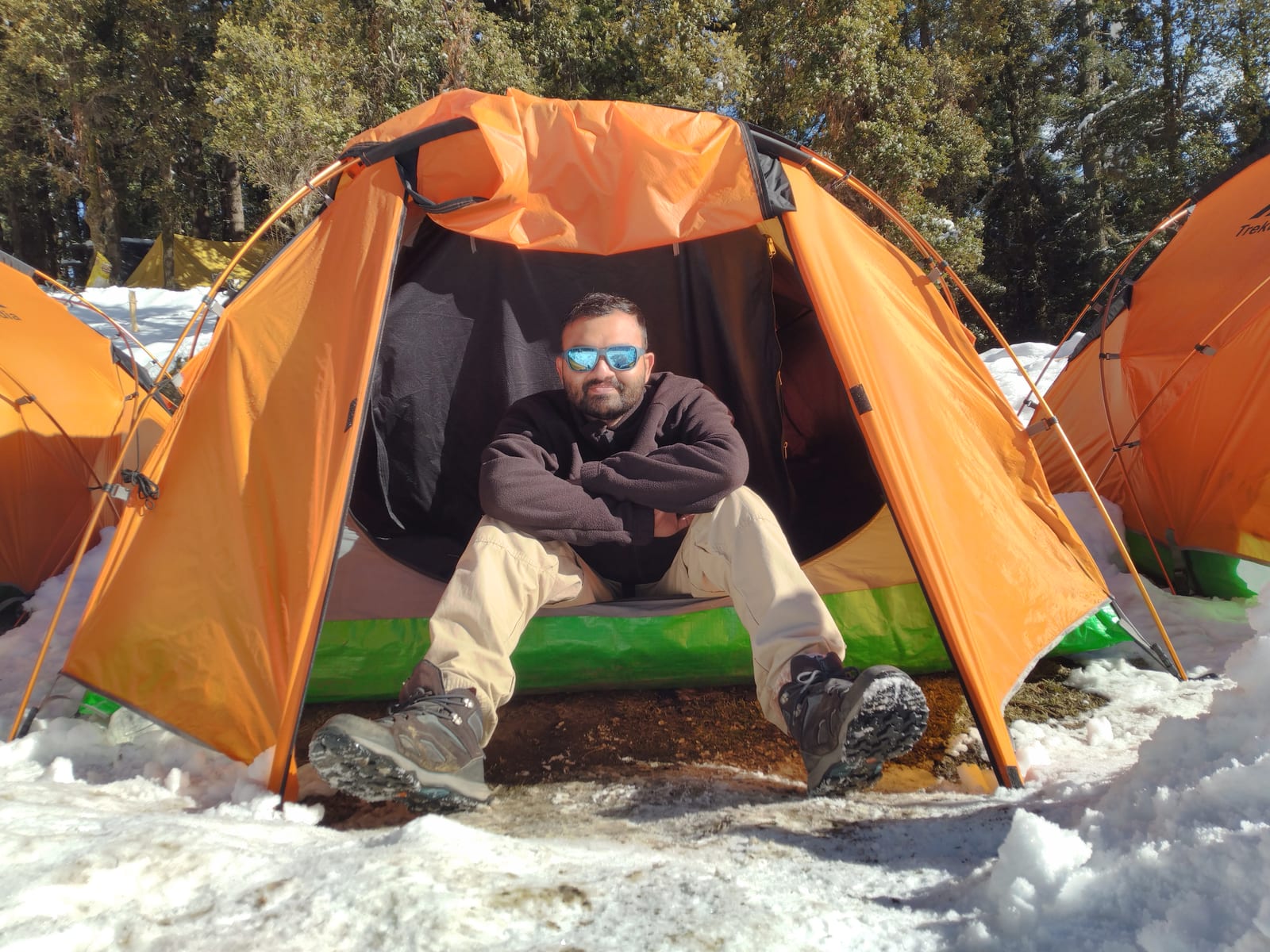 Priyank sitting at the entrance of an orange tent in snow