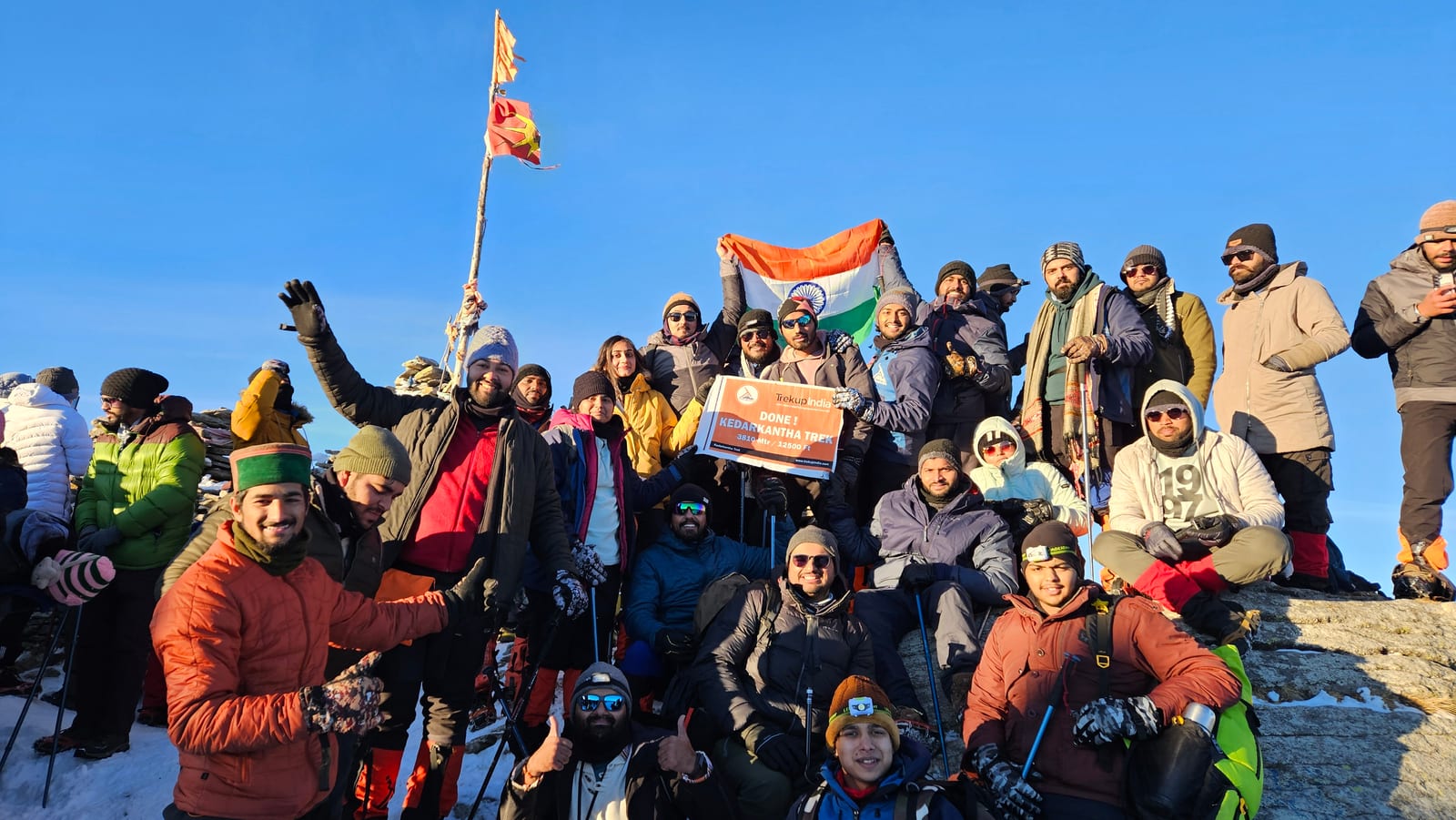 Group celebrating with a flag at Kedarkantha summit